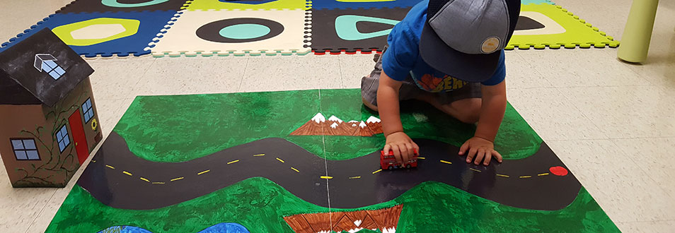 A child playing with a toy truck over a play mat decorated like a road and a green field